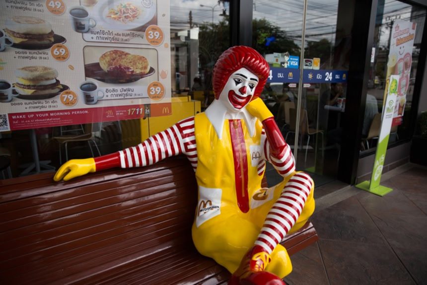 Statue de Ronald McDonald assise sur un banc devant un restaurant